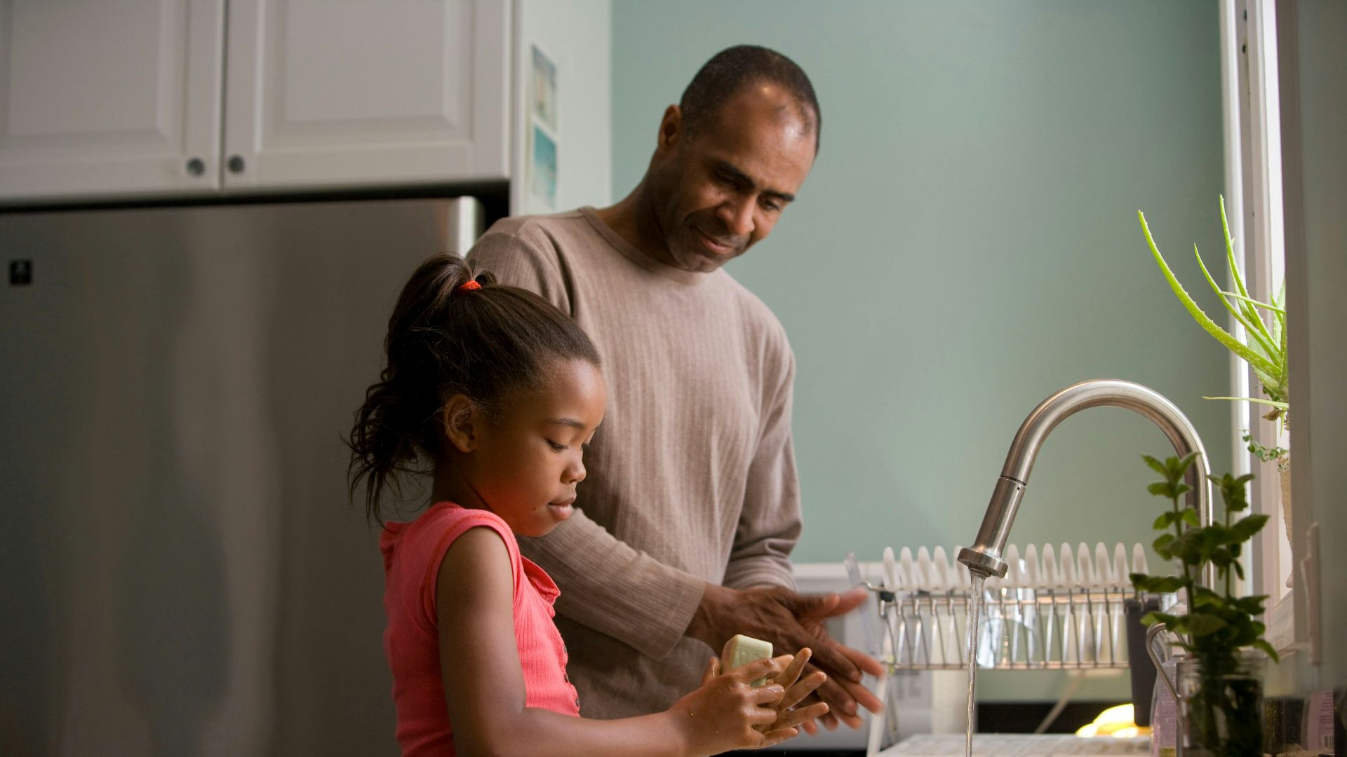 man in long sleeve shirt standing beside girl in pink tank top washing hands