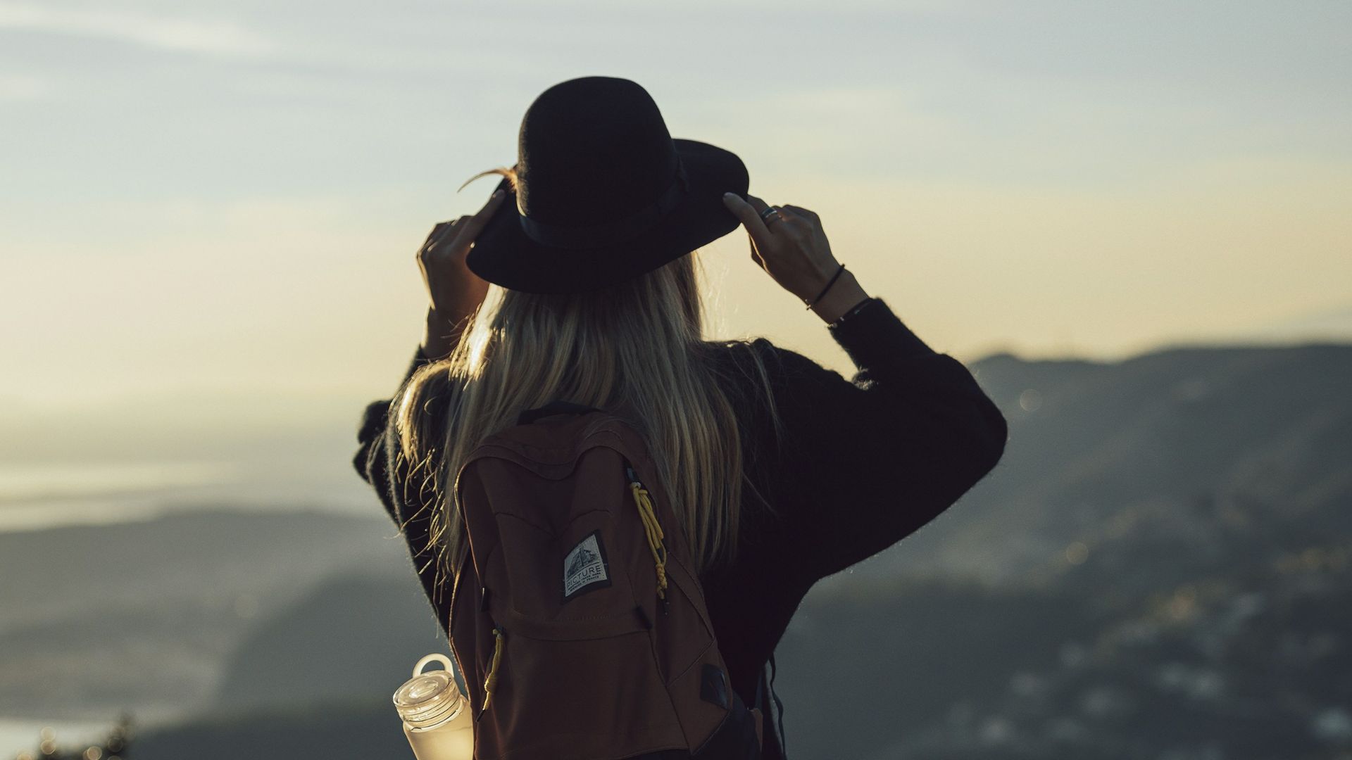 woman in gray hoodie and black pants wearing black hat standing on top of mountain during