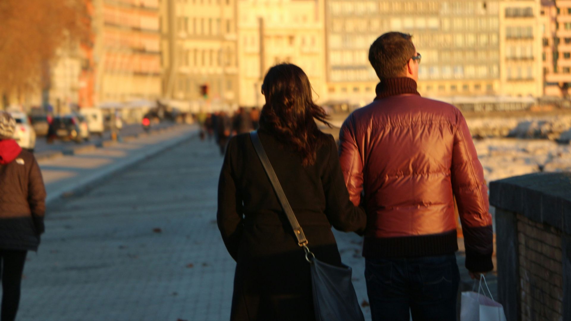 Couple walking along a waterfront with buildings.