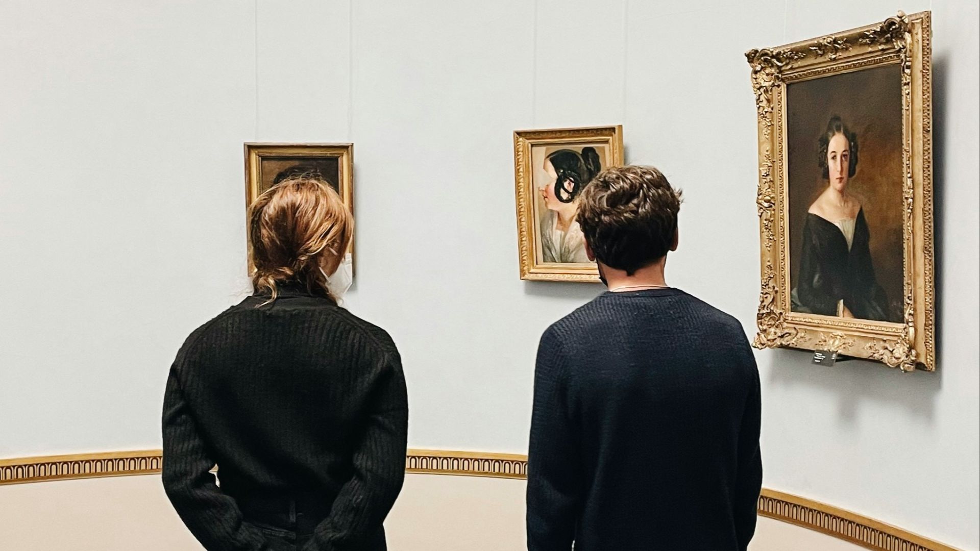 a man and woman looking at paintings in a museum