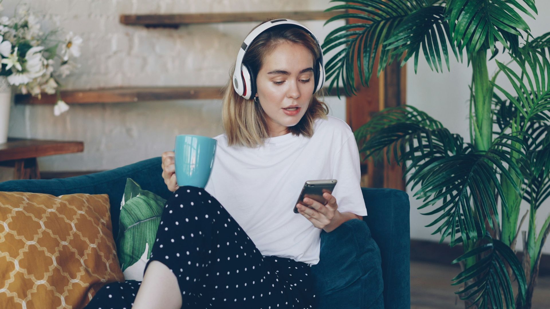 Woman listening to music on phone while holding mug.