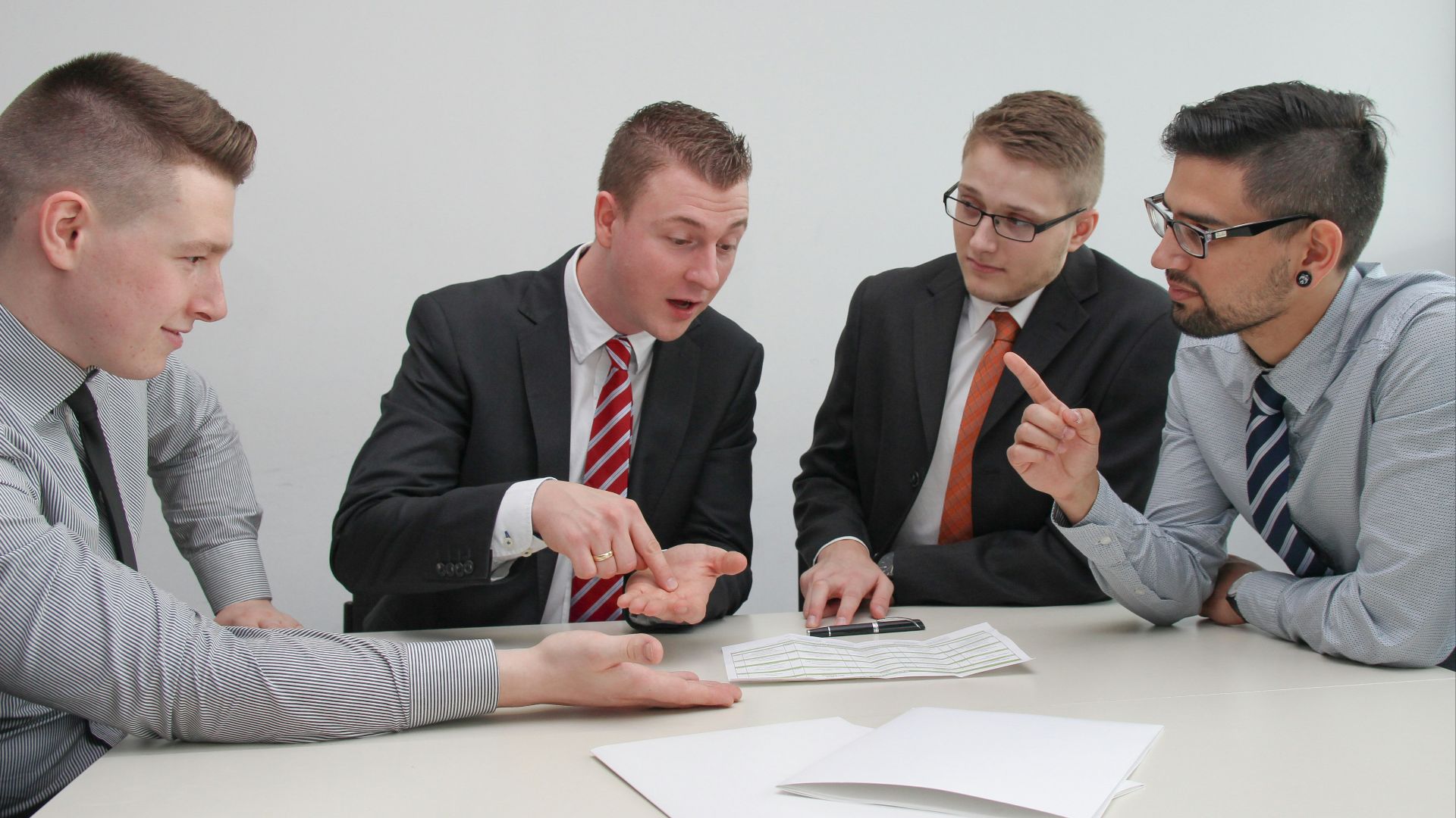 four men sitting at desk talking