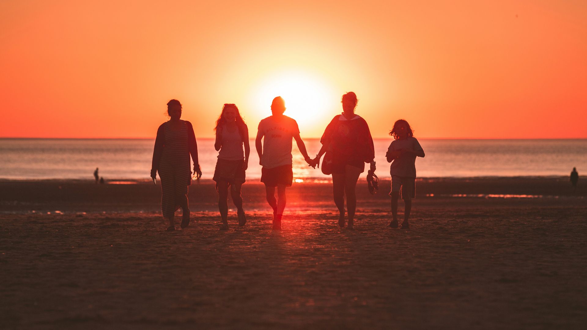 silhouette photo of five person walking on seashore during golden hour