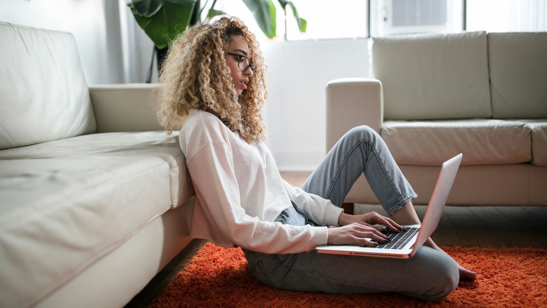 woman sitting on floor and leaning on couch using laptop