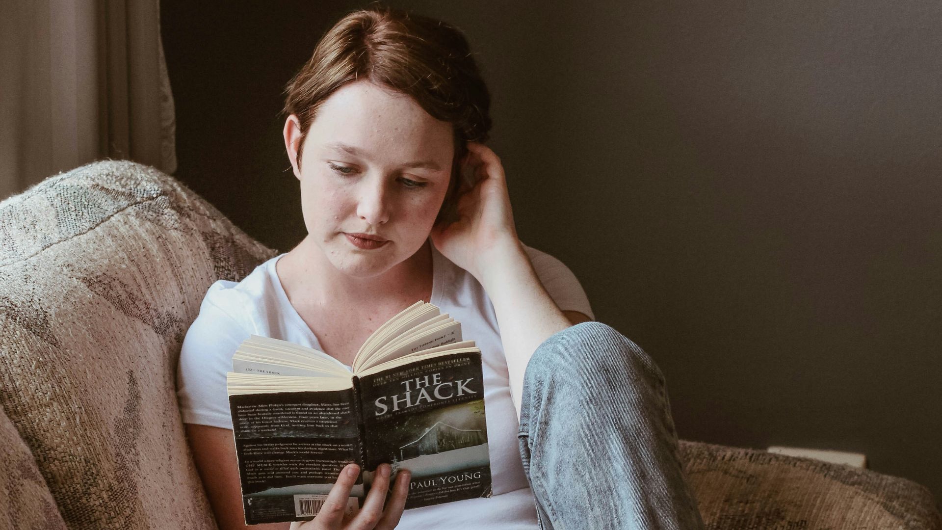 woman sitting on sofa while reading book inside room