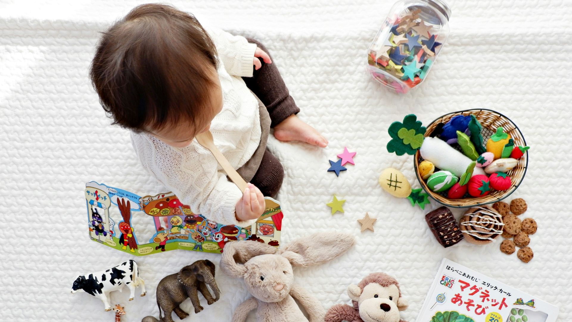 boy sitting on white cloth surrounded by toys