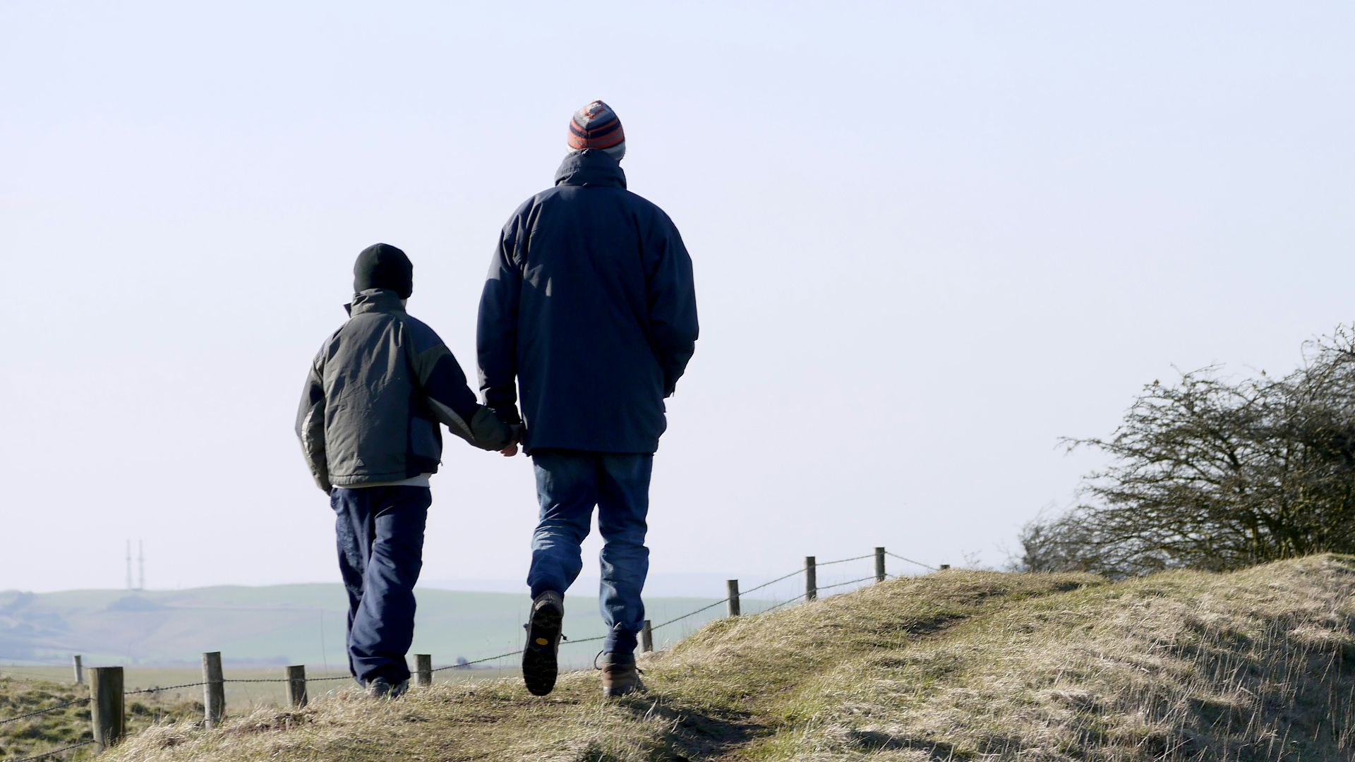 man and boy walking on grass near fence