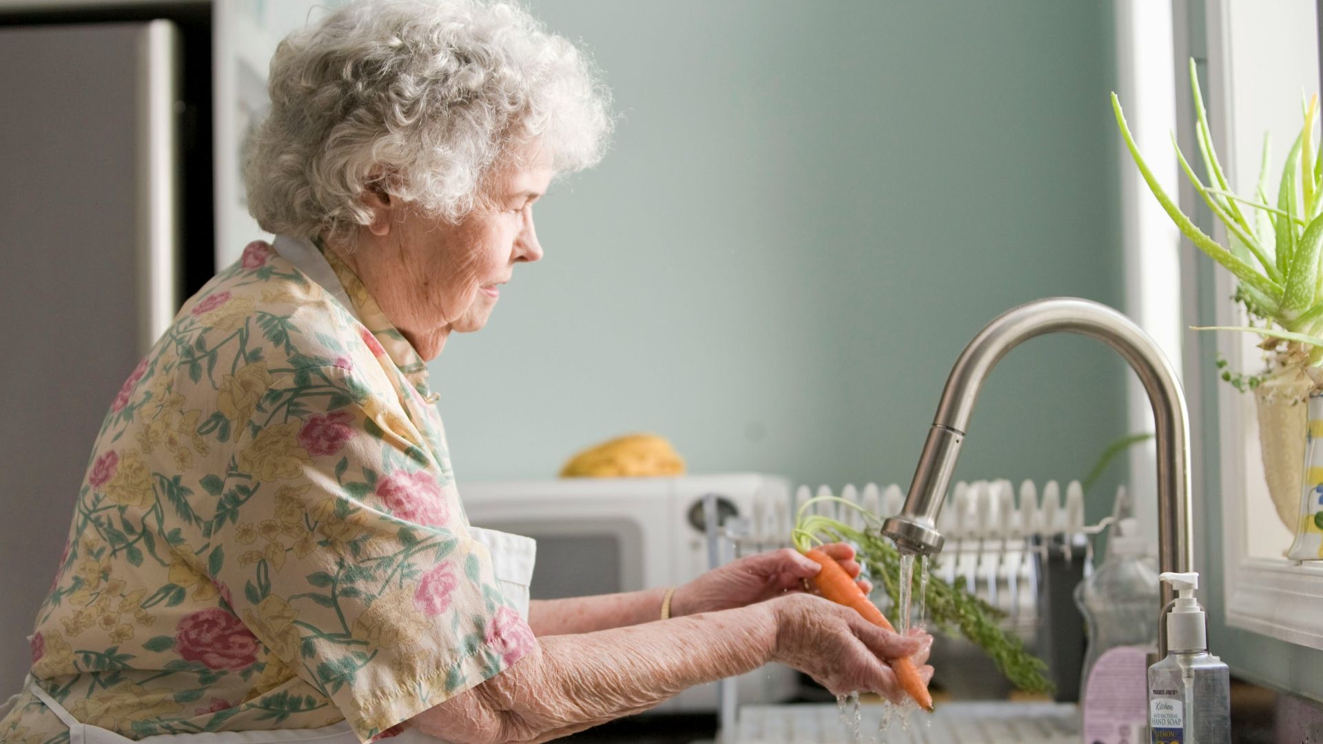 woman wearing yellow and pink floral dress wahing carrots