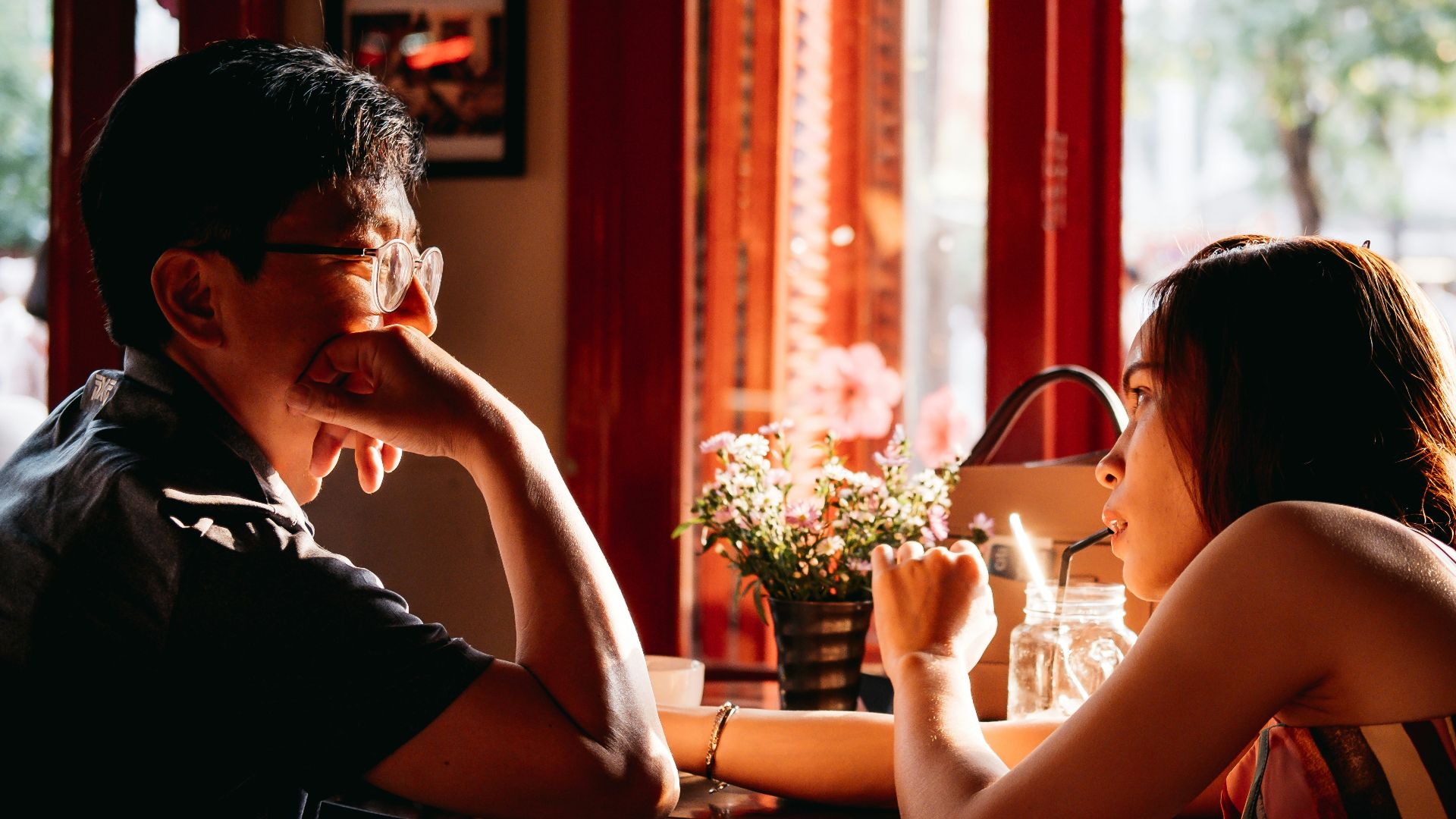 man wearing black collared top sitting on chair in front of table and woman wearing multicolored top