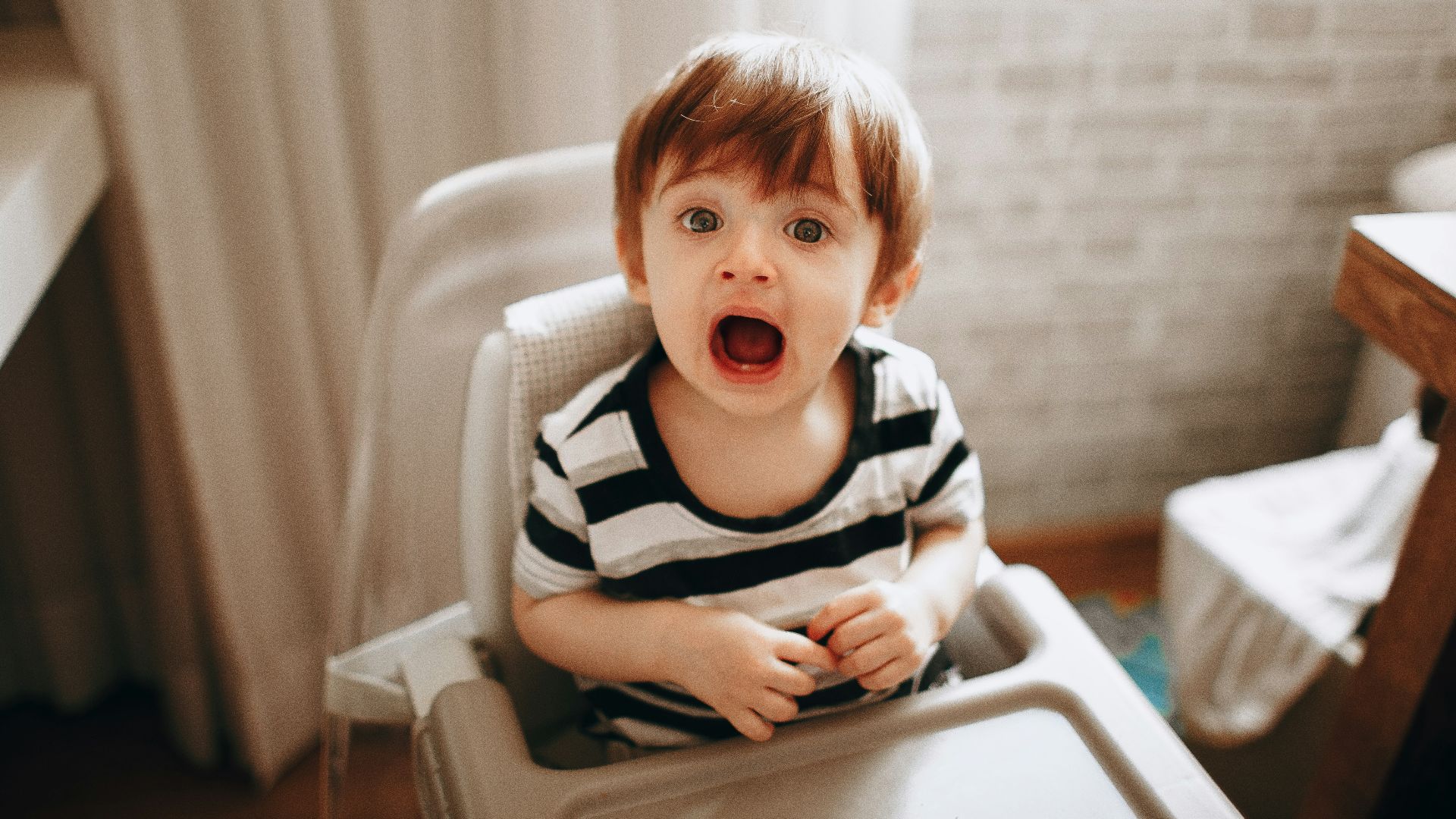 boy in black and white striped shirt sitting on white high chair