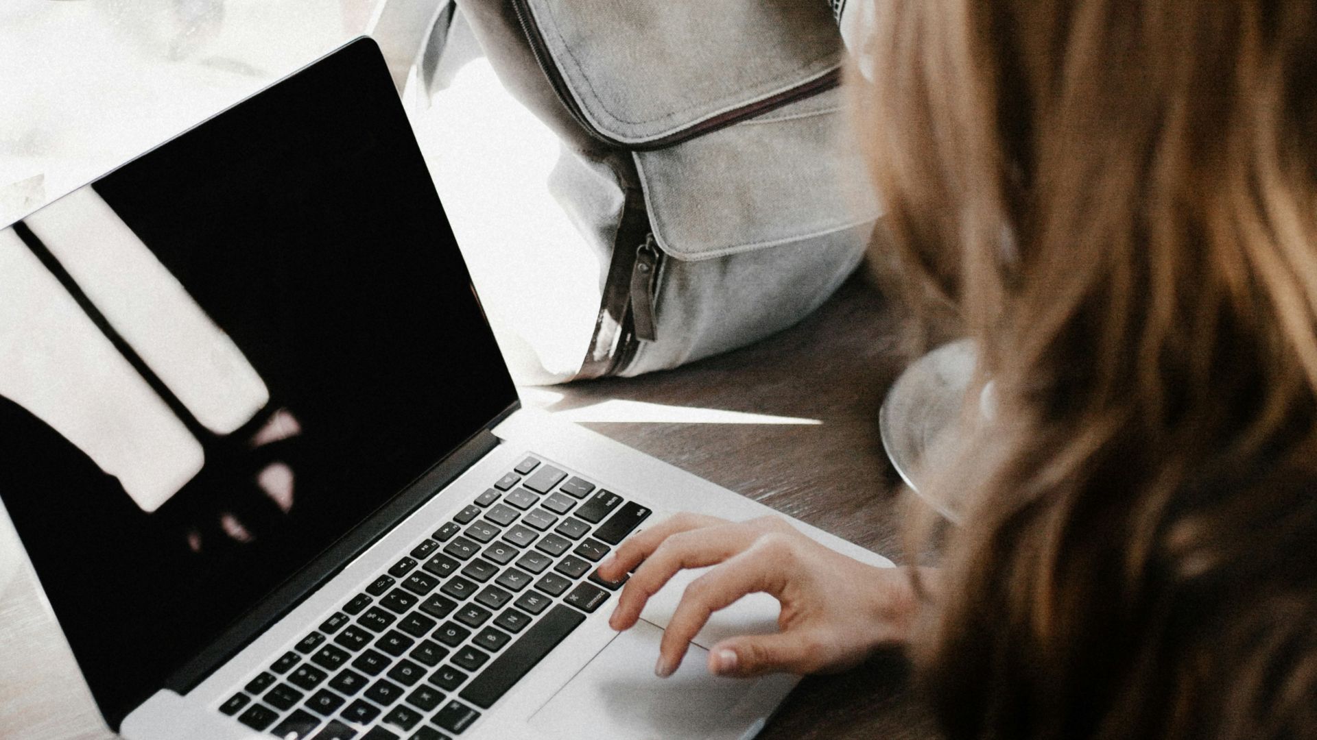 girl wearing grey long-sleeved shirt using MacBook Pro on brown wooden table