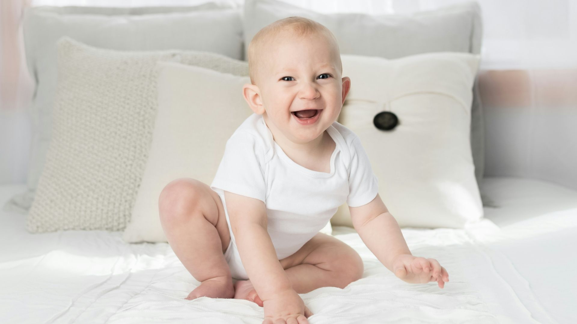 smiling baby sitting on white bed