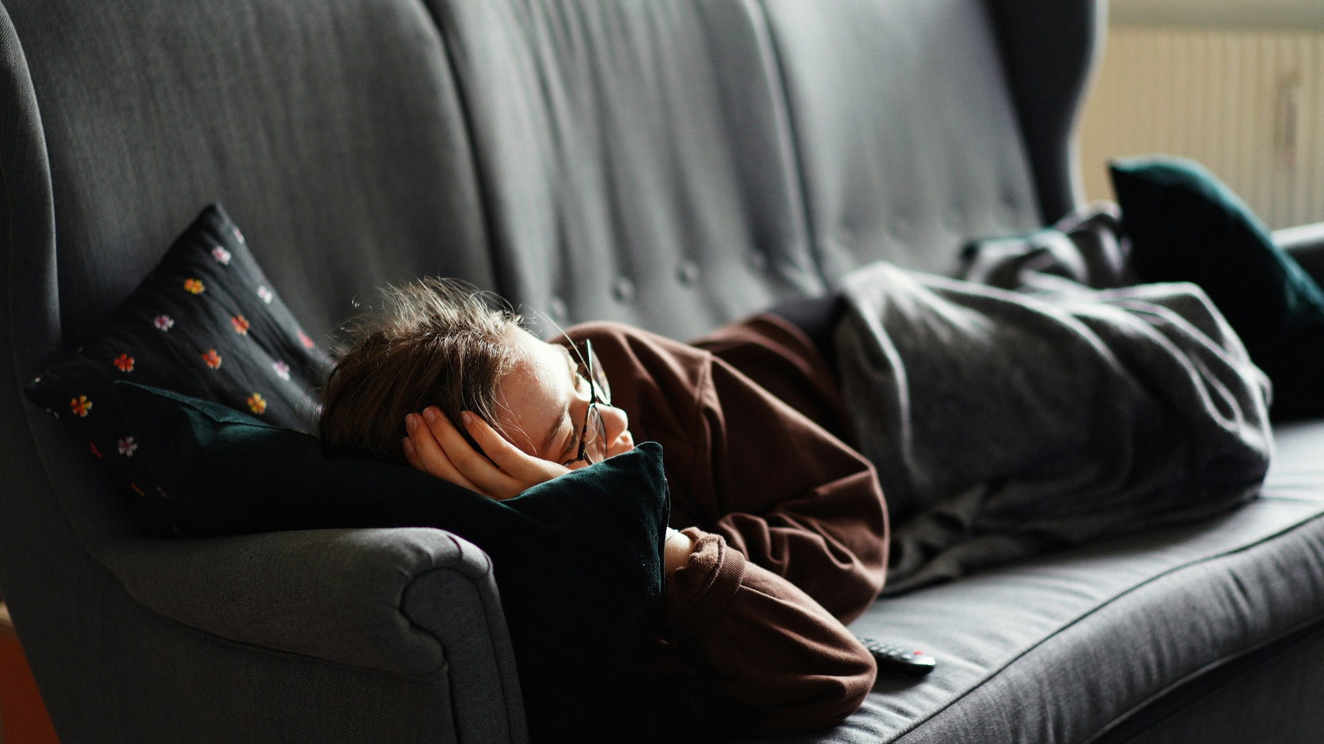 woman in pink jacket lying on gray couch