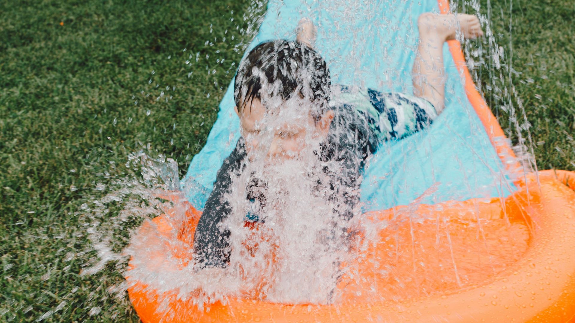 child sliding on blue and orange slippery pad with water splash at daytime