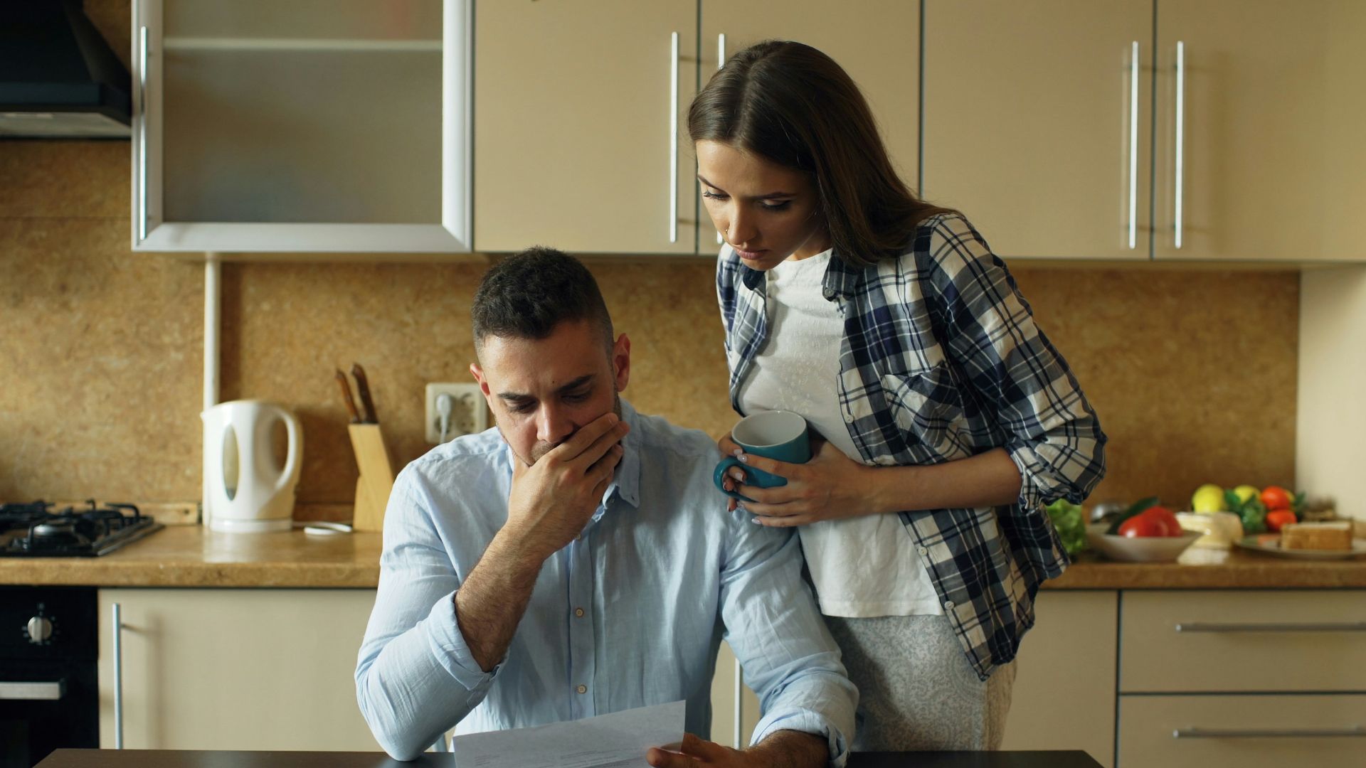 Couple looking stressed over bills at kitchen table.