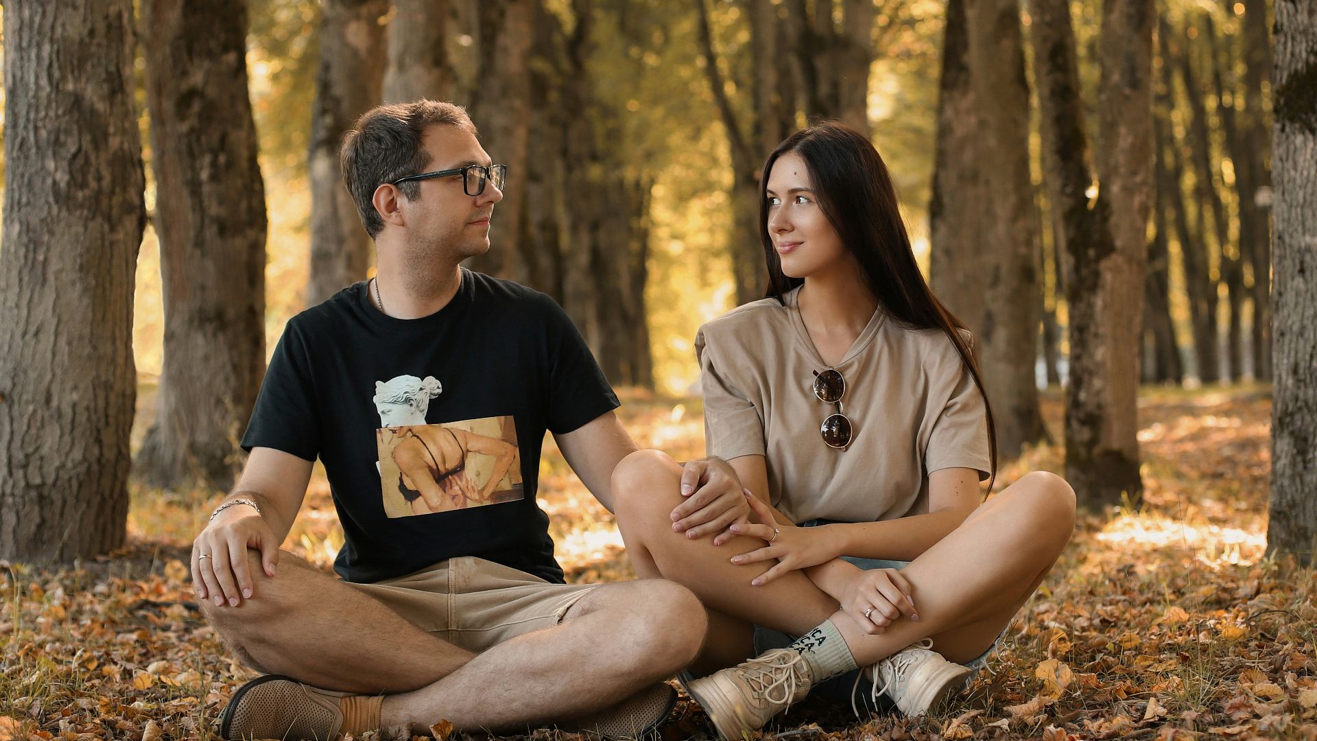 a man and a woman sitting on the ground in a forest