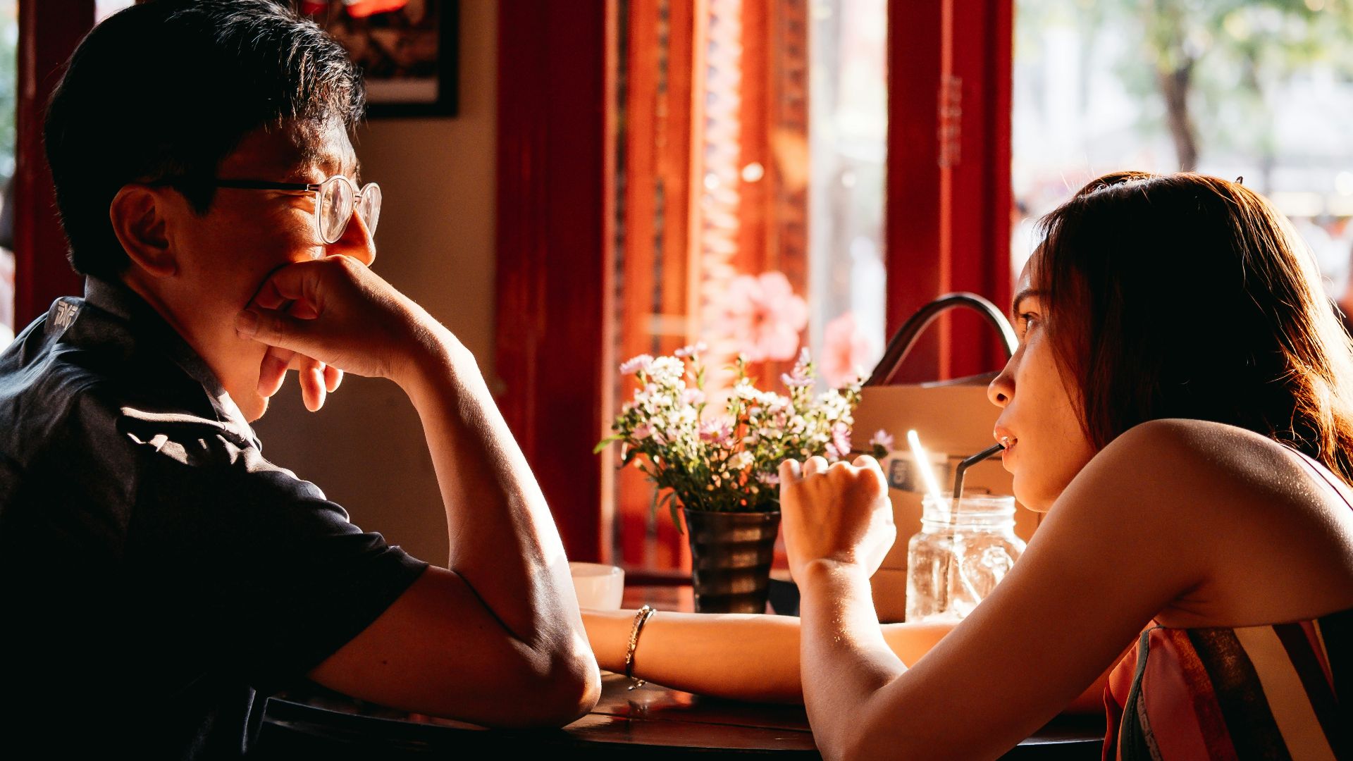 man wearing black collared top sitting on chair in front of table and woman wearing multicolored top