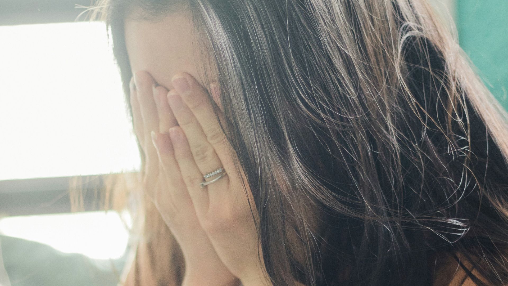 woman in brown shirt covering her face