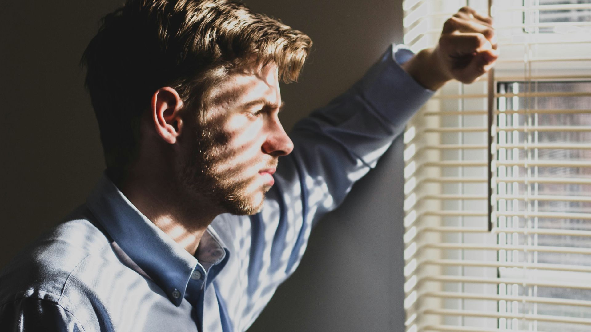 person near clear glass window pane and window blinds low-light photography