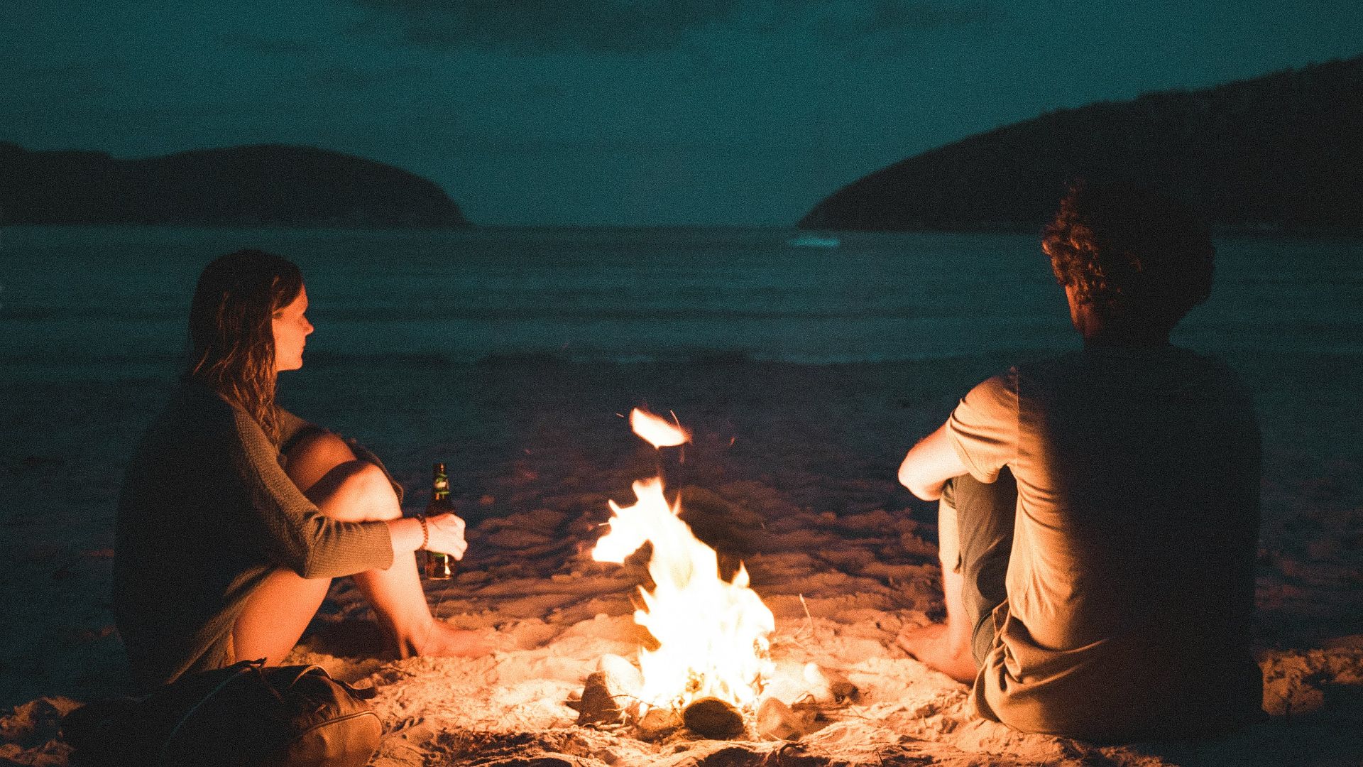 man and woman with bone fire sitting on seashore