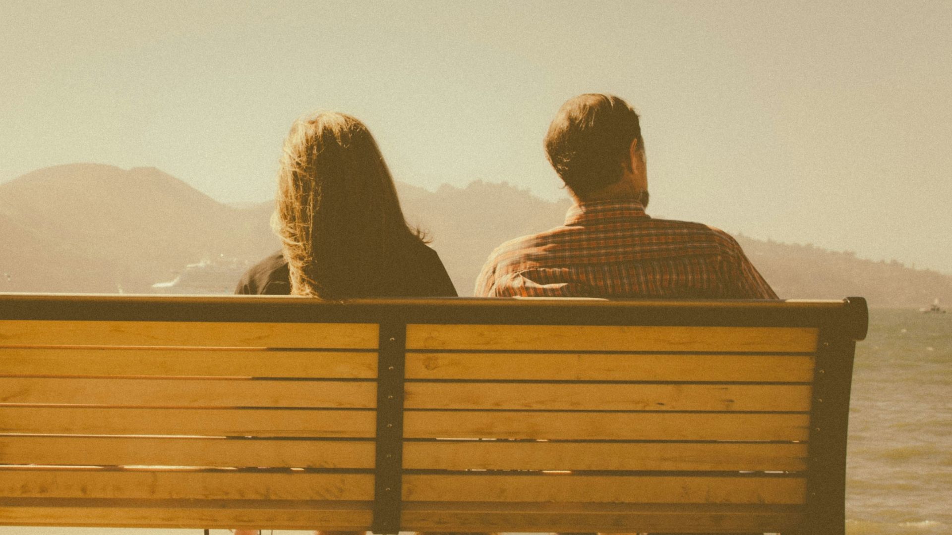 man and woman sitting on bench beside body of water