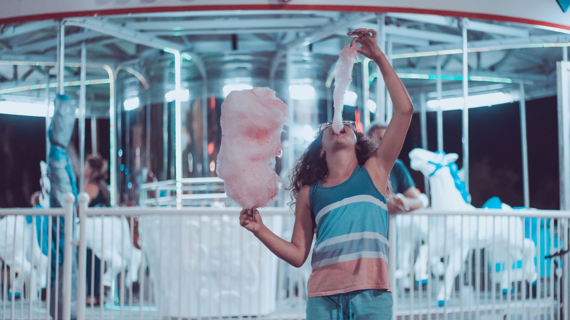 woman eating pink cotton candy beside carousel
