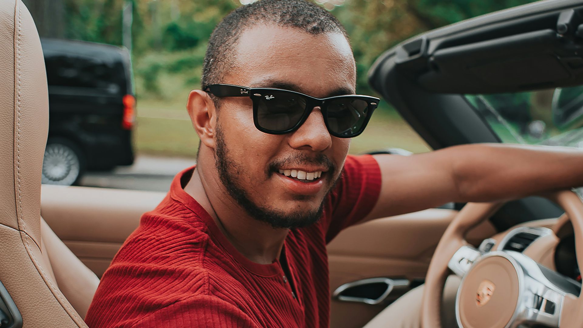 man in red crew neck shirt wearing black sunglasses sitting on driver seat