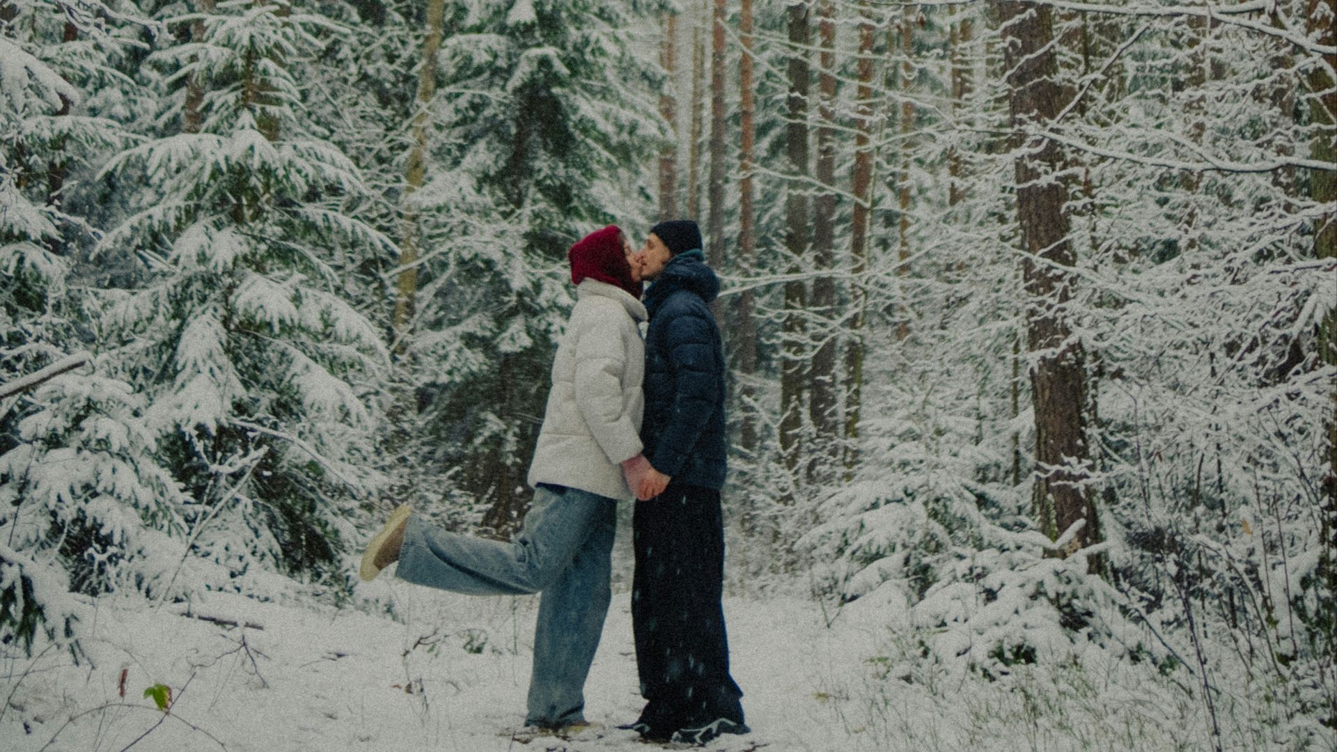 Couple kissing in a snowy forest with tall trees