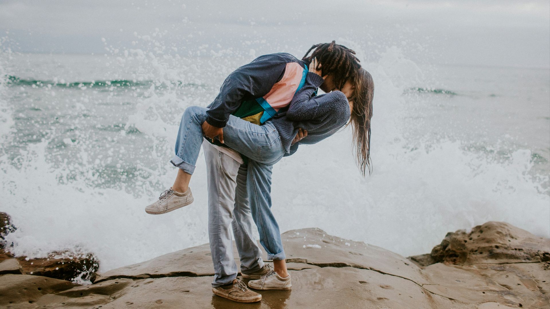 woman in blue jacket and gray pants carrying woman in blue jacket on beach during daytime