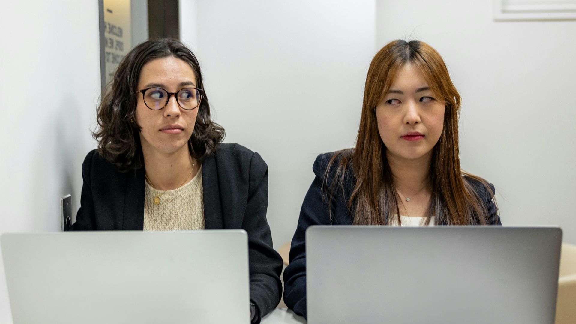 two women sitting at a table with laptops