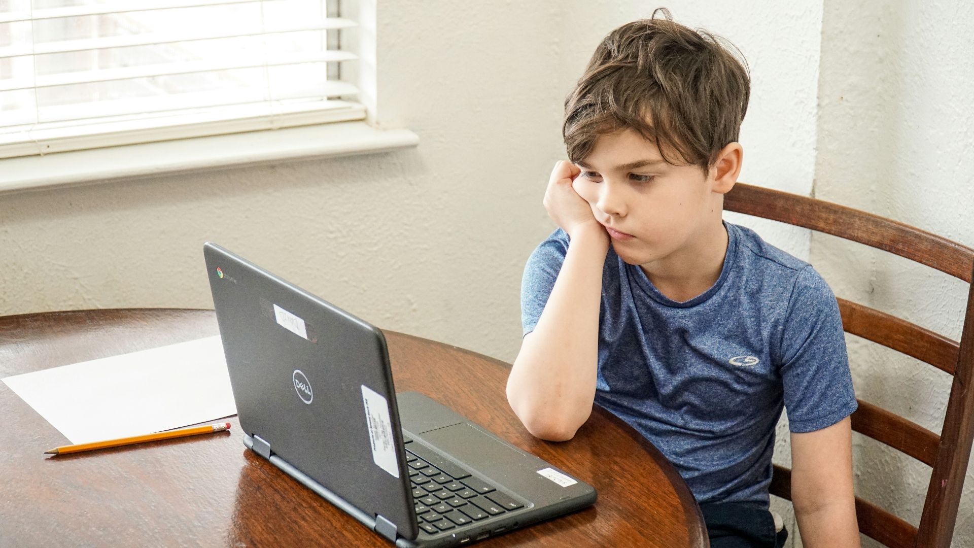 boy in blue crew neck t-shirt using macbook pro on brown wooden table