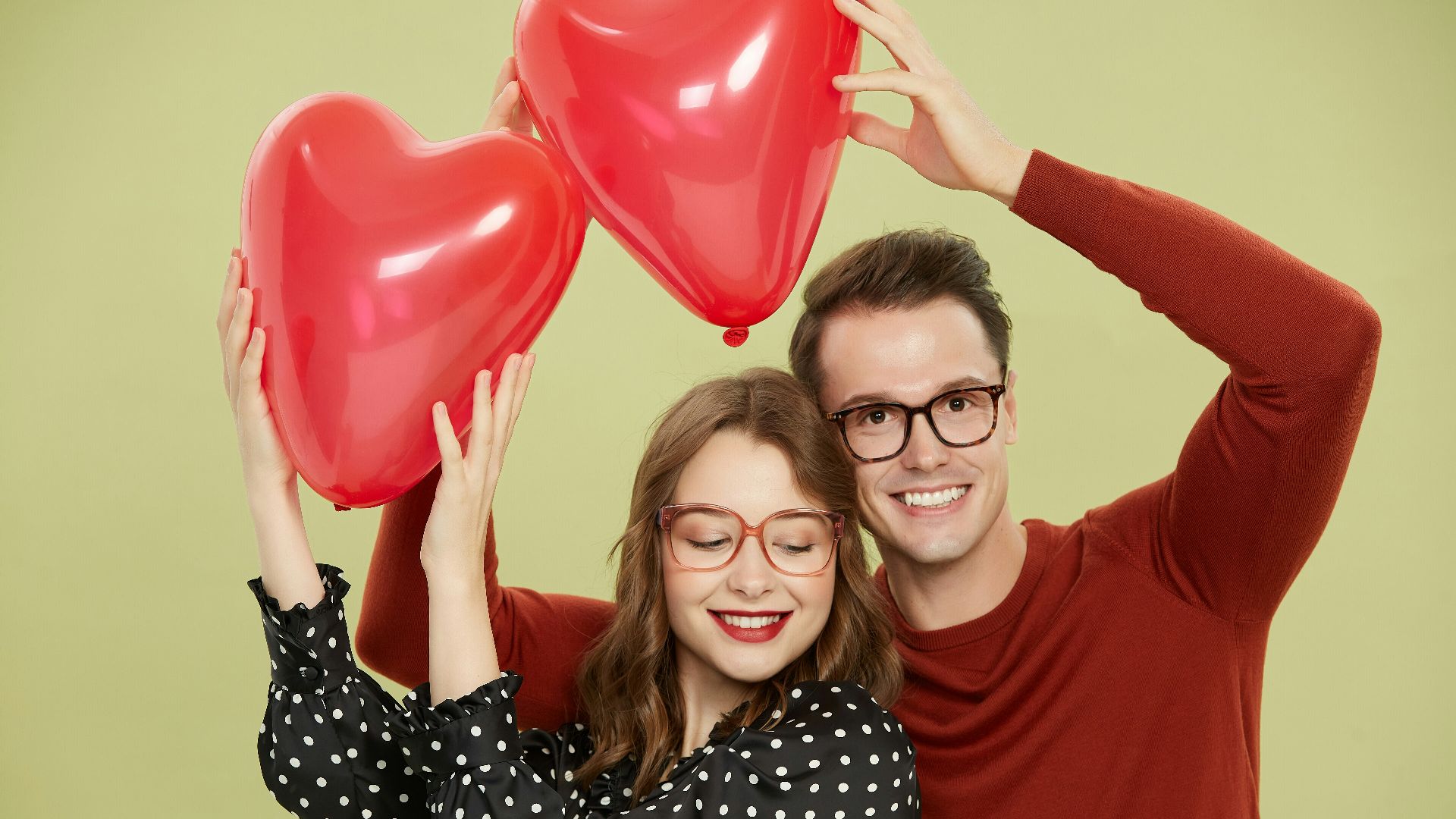 A man and a woman holding red heart shaped balloons
