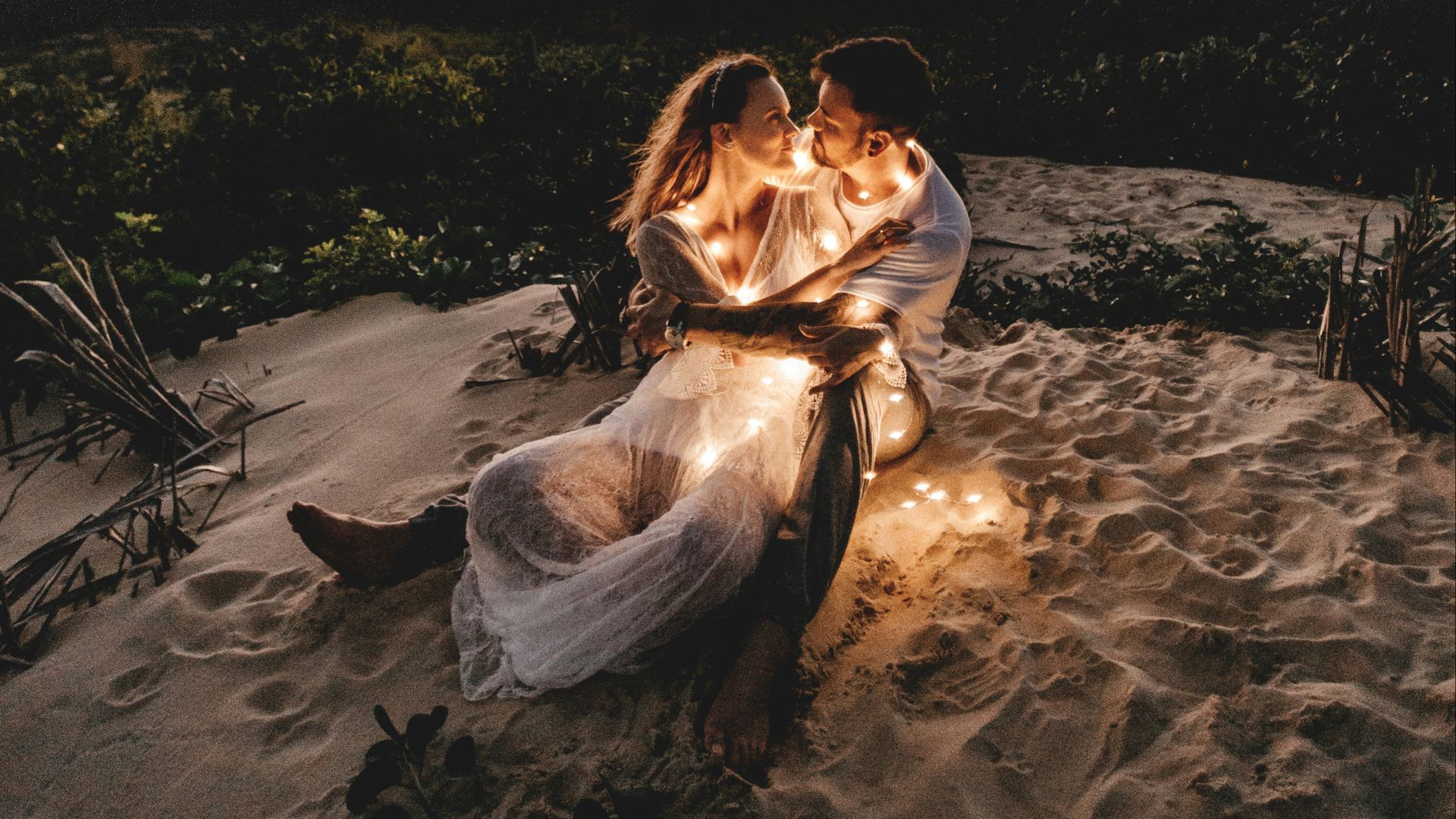 man and woman looking each other sitting on white sand during sunset