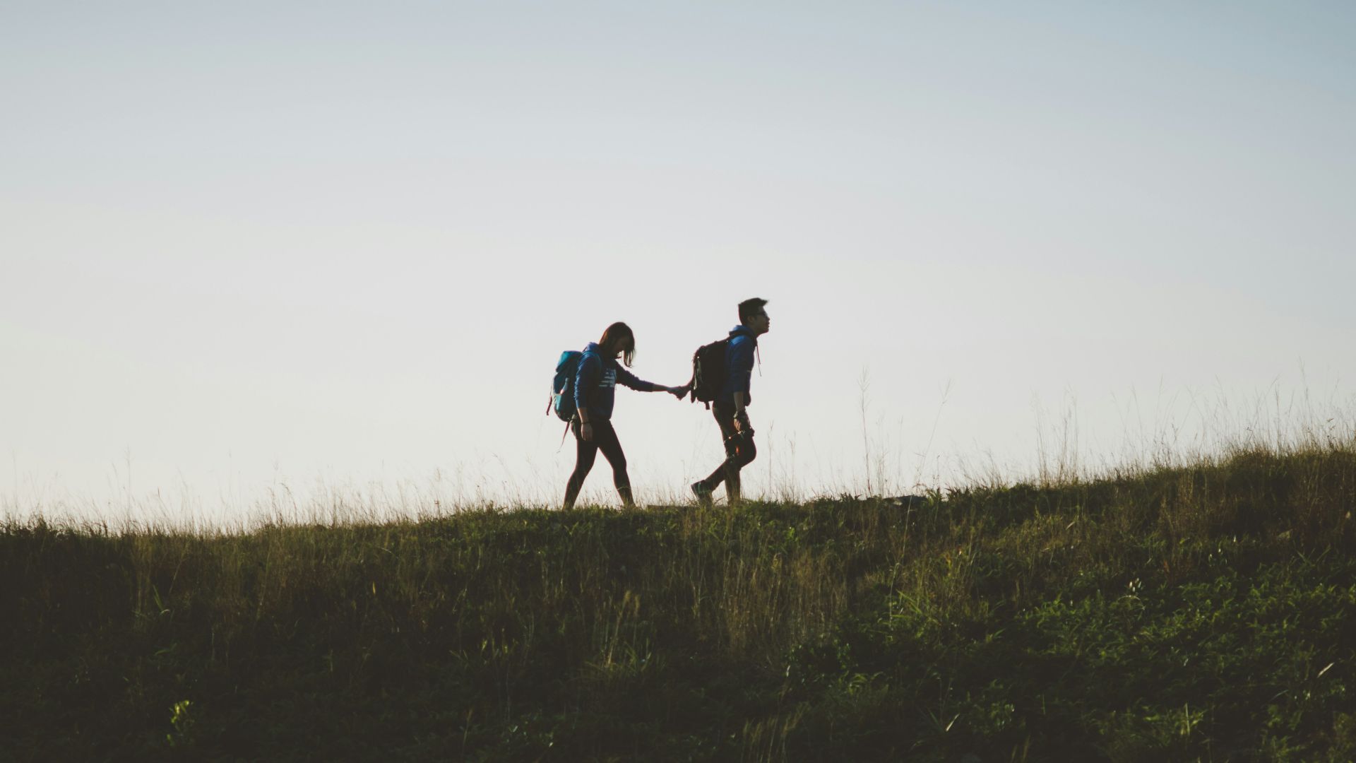 couple walking on hill while holding during daytime