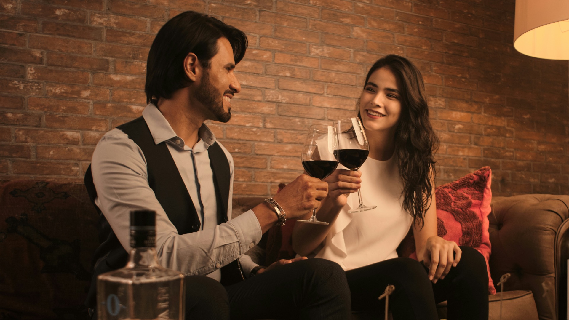 a man and a woman sitting on a couch holding wine glasses