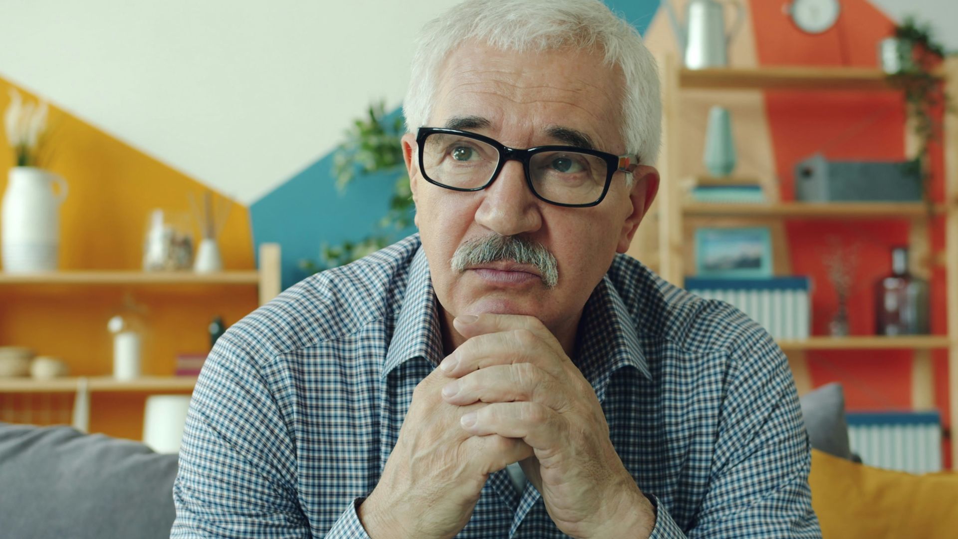 Elderly man with glasses resting chin on hands.