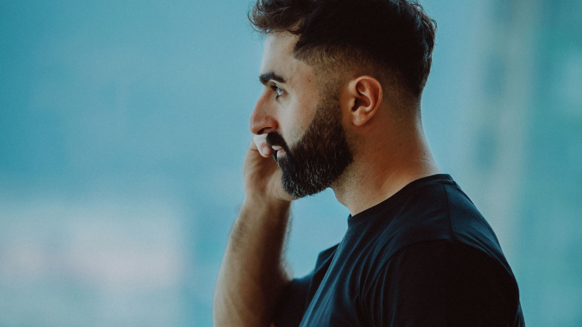 Man with beard talking on cell phone near window