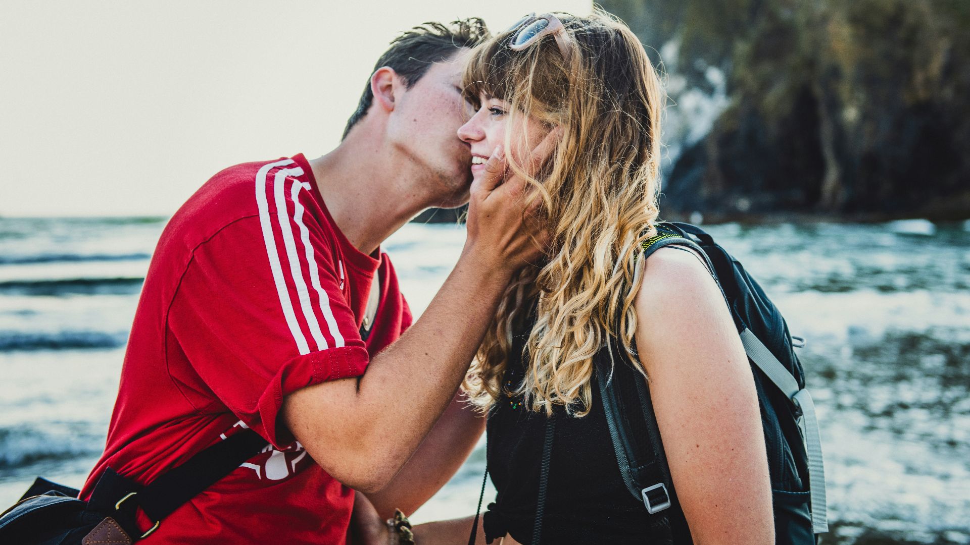 man wearing red crew-neck shirt kissing woman wearing black top