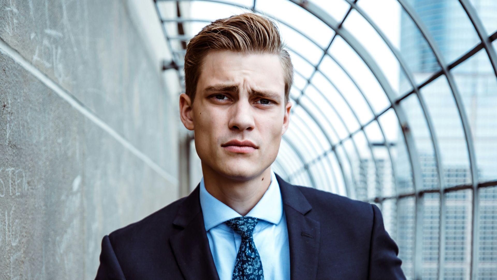 man wearing black and teal dress suit standing near gray wall