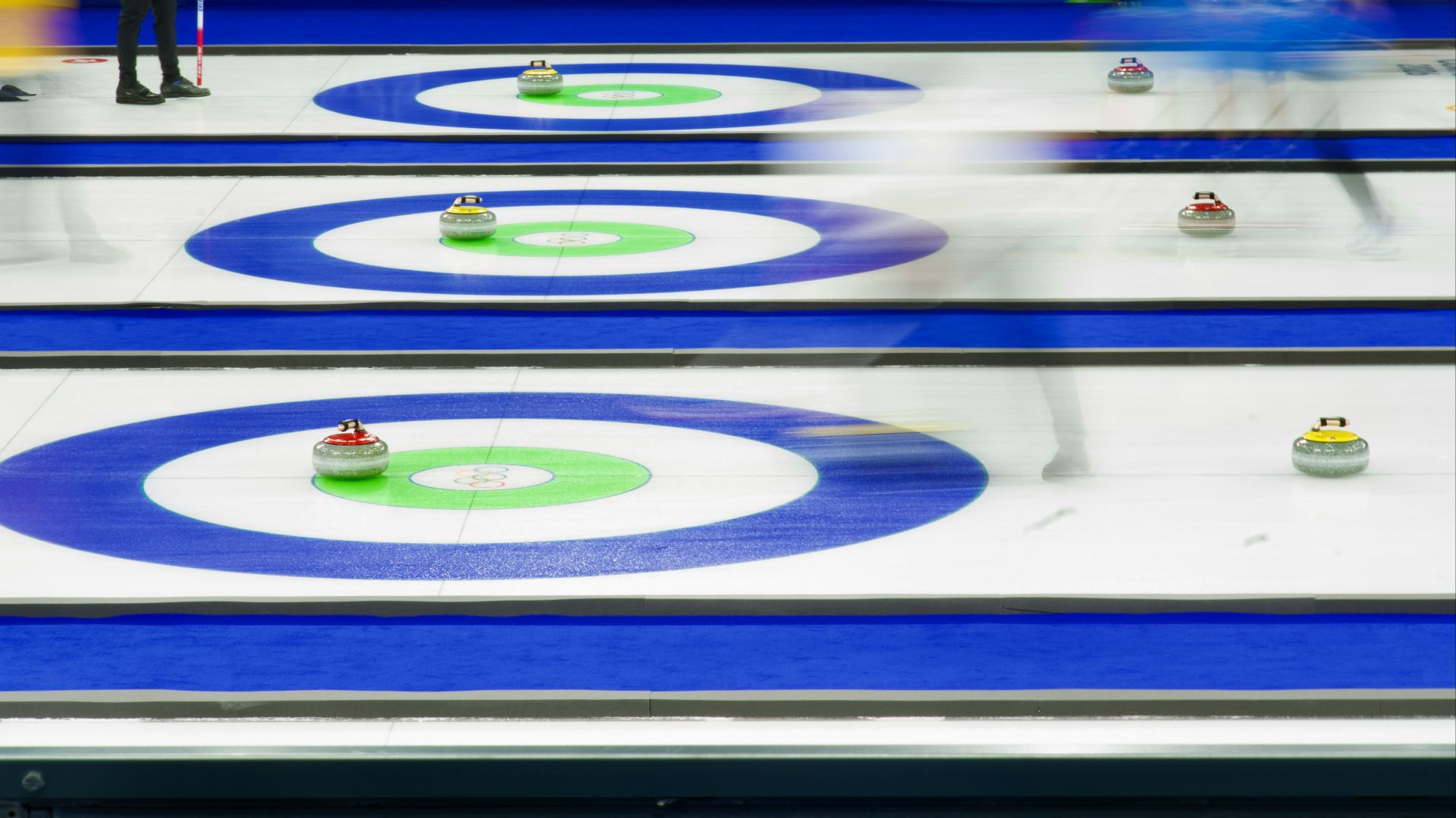 Curling match with athletes sliding stones on ice.