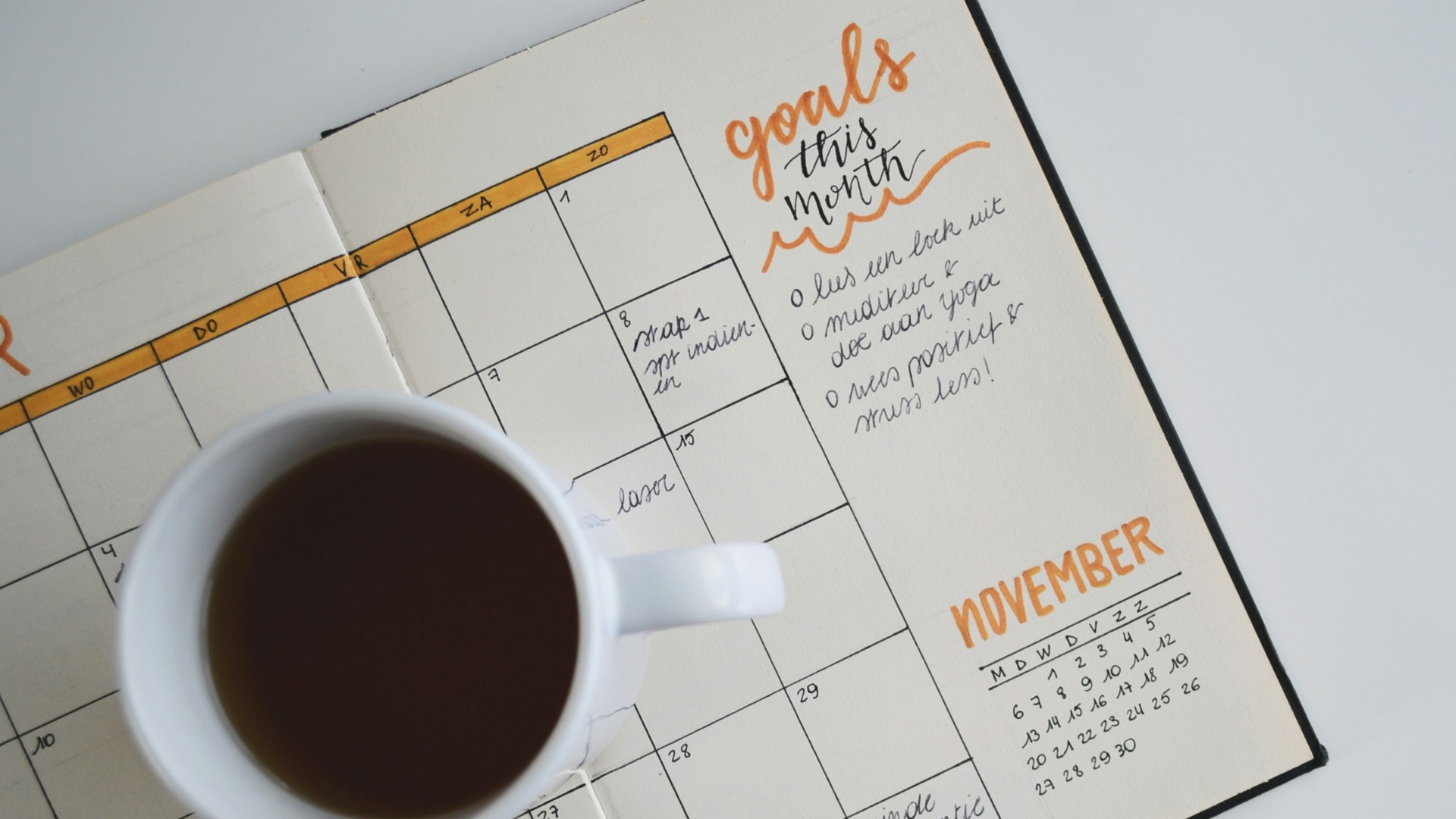 white ceramic mug with coffee on top of a planner