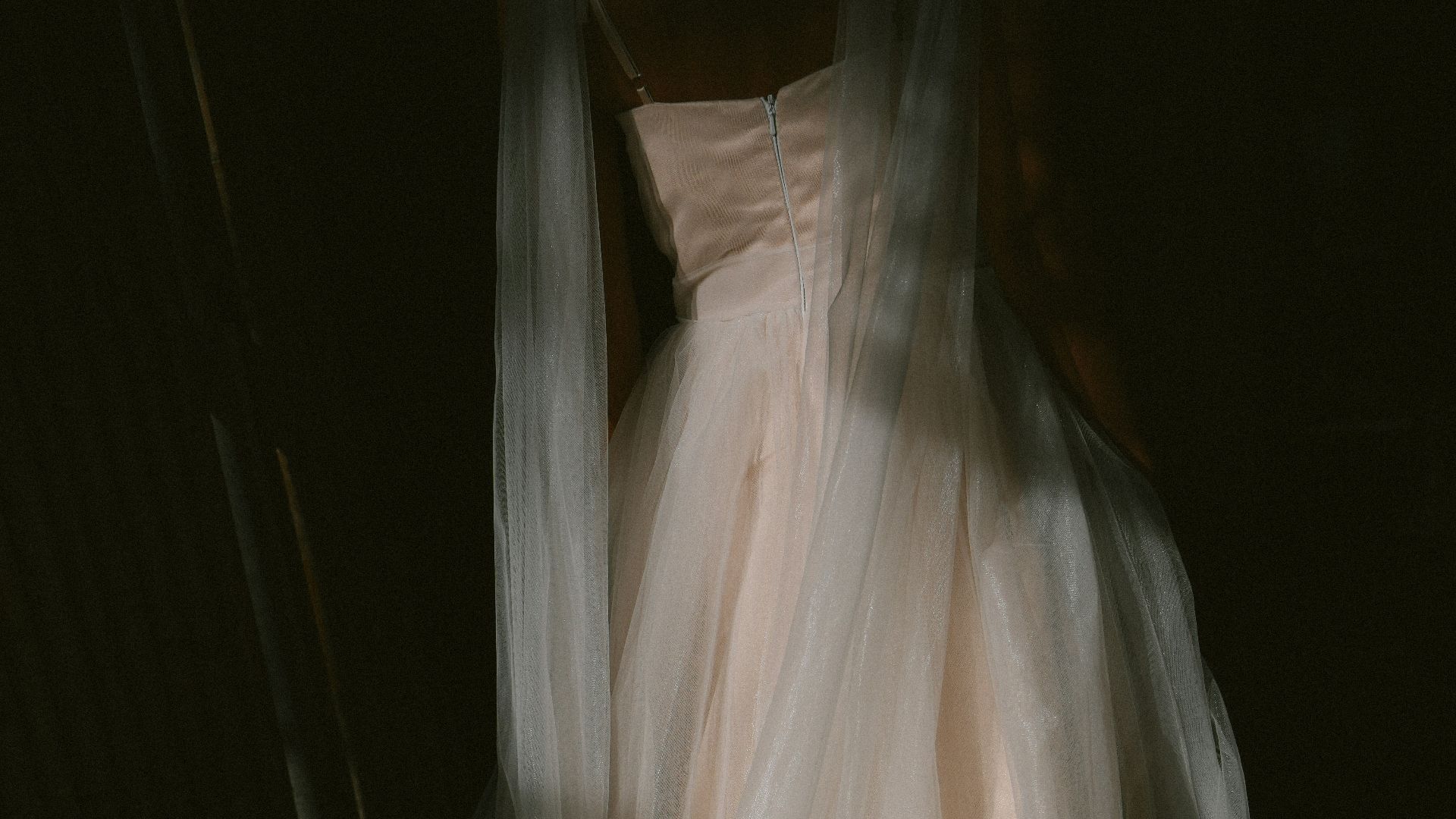 A delicate wedding dress hangs outdoors at night.