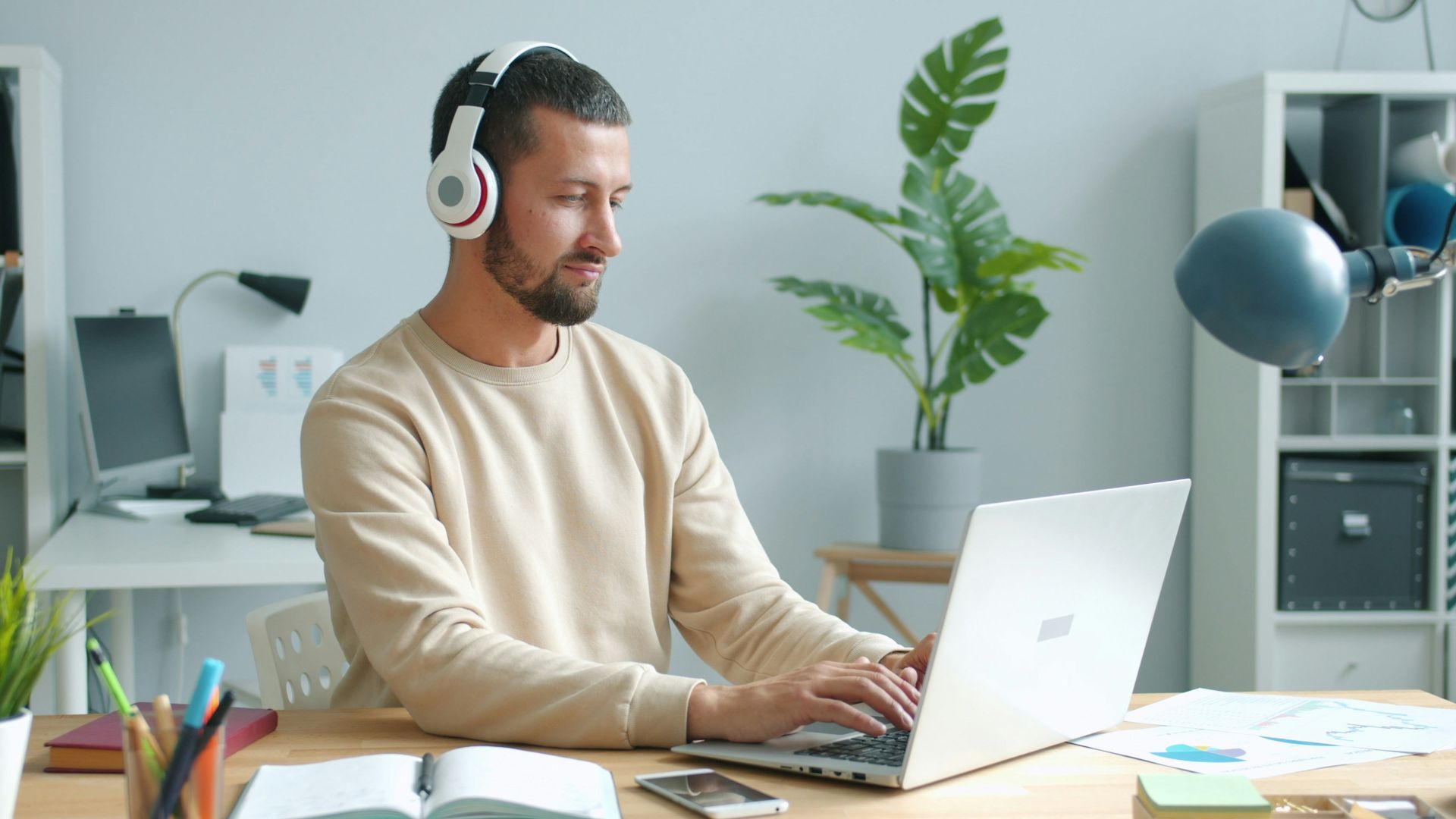 Man wearing headphones works on laptop at desk.