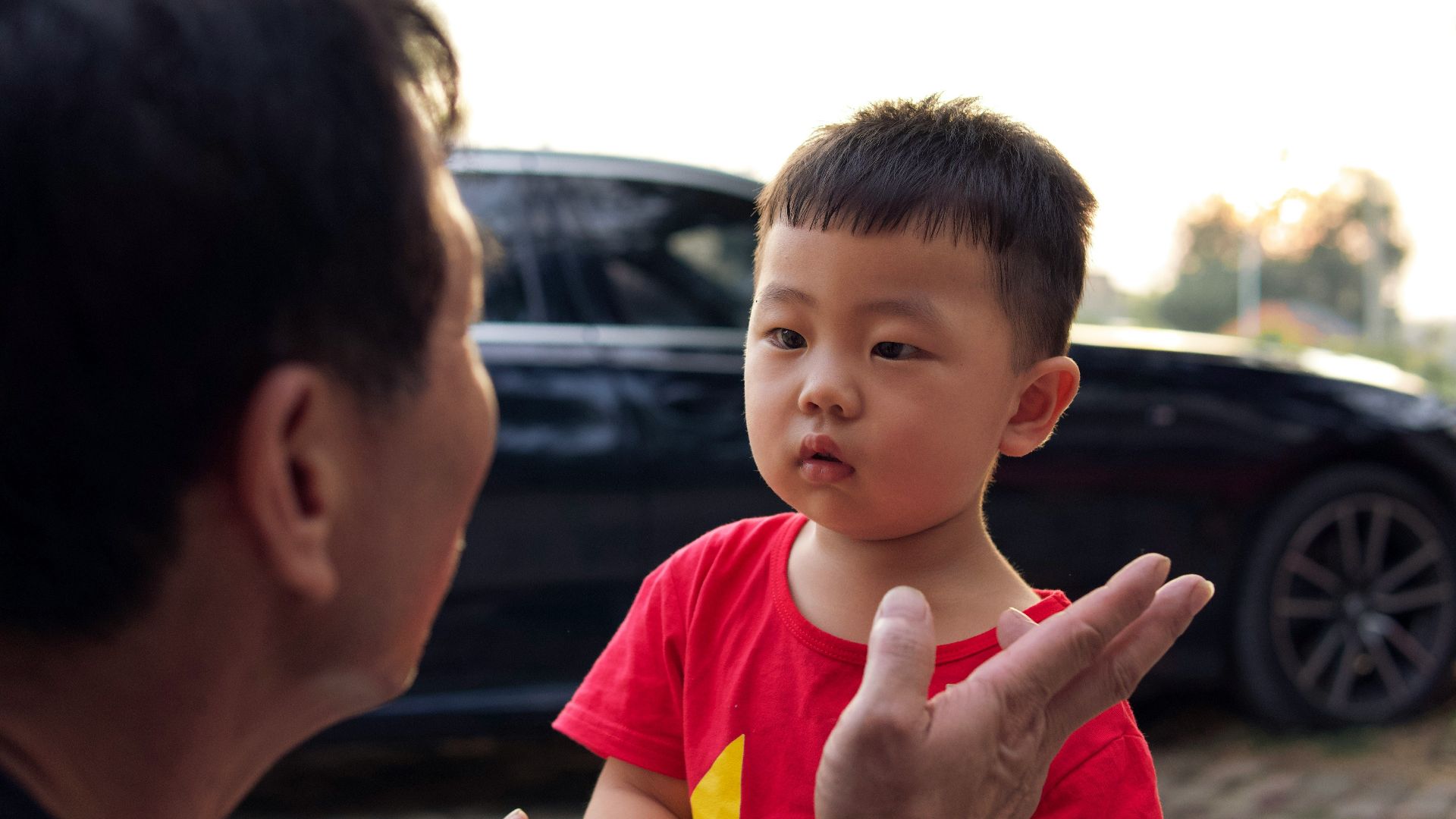 a man talking to a little boy in front of a car
