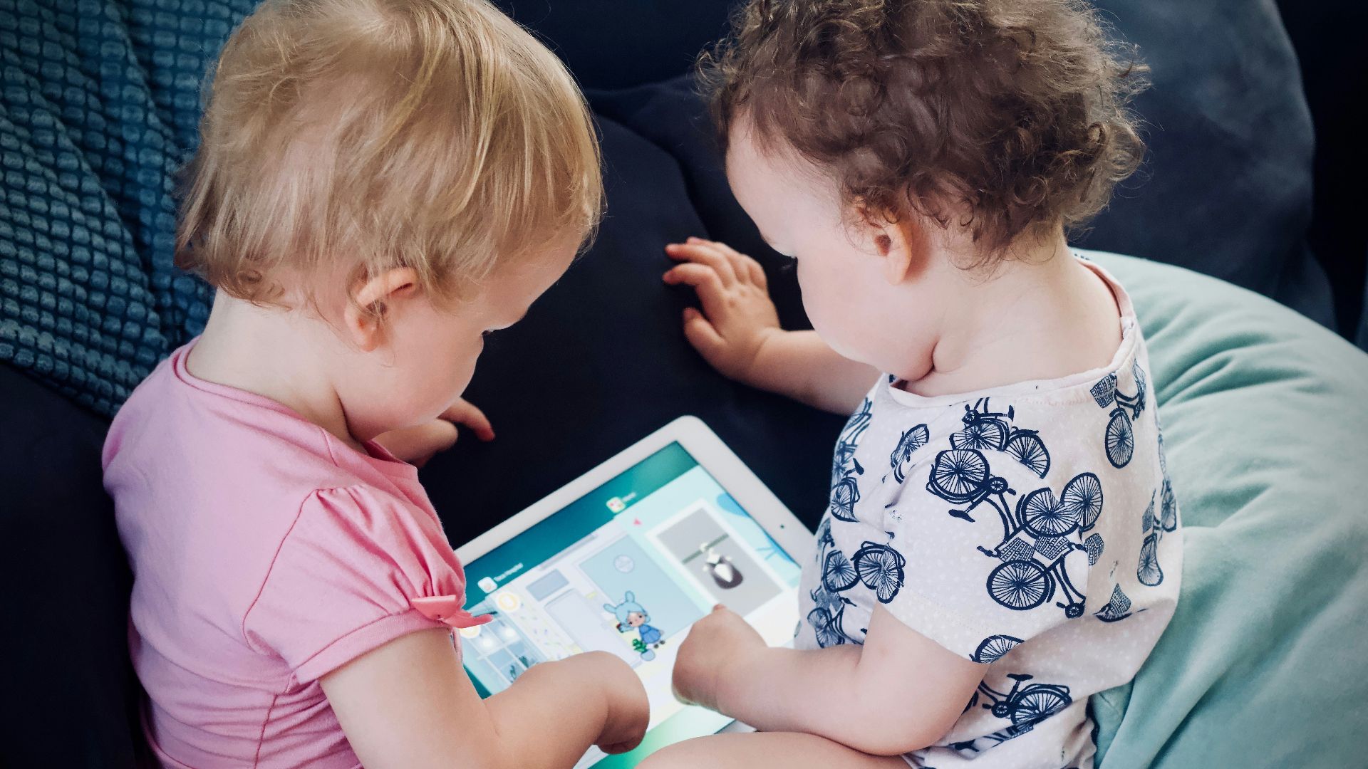 two toddlers sitting on sofa while using tablet computer