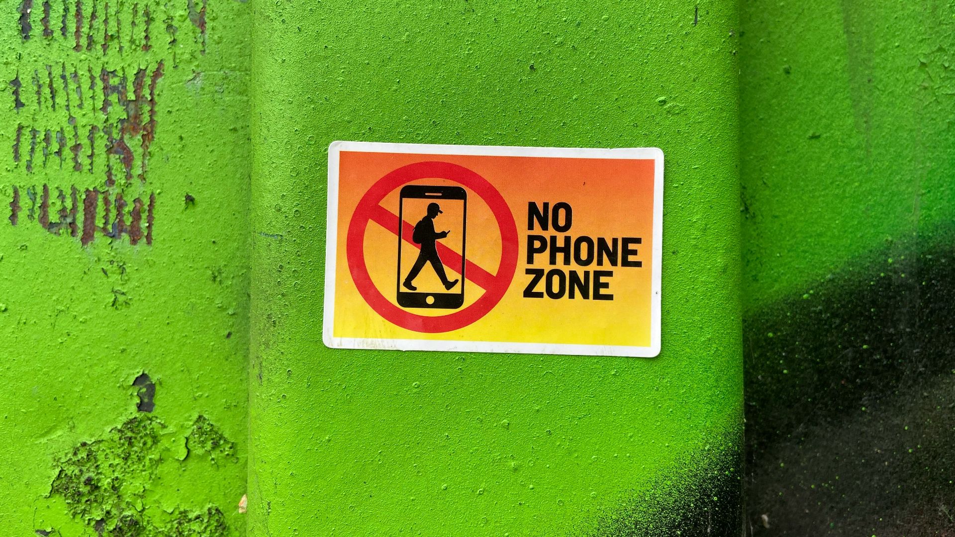 A no phone zone sign on a green wall