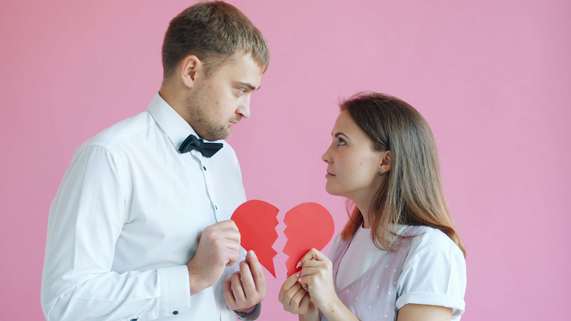 Couple holding broken heart halves on pink background