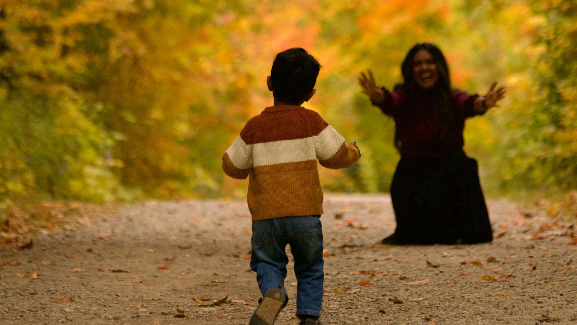 Child running towards a woman in autumn forest