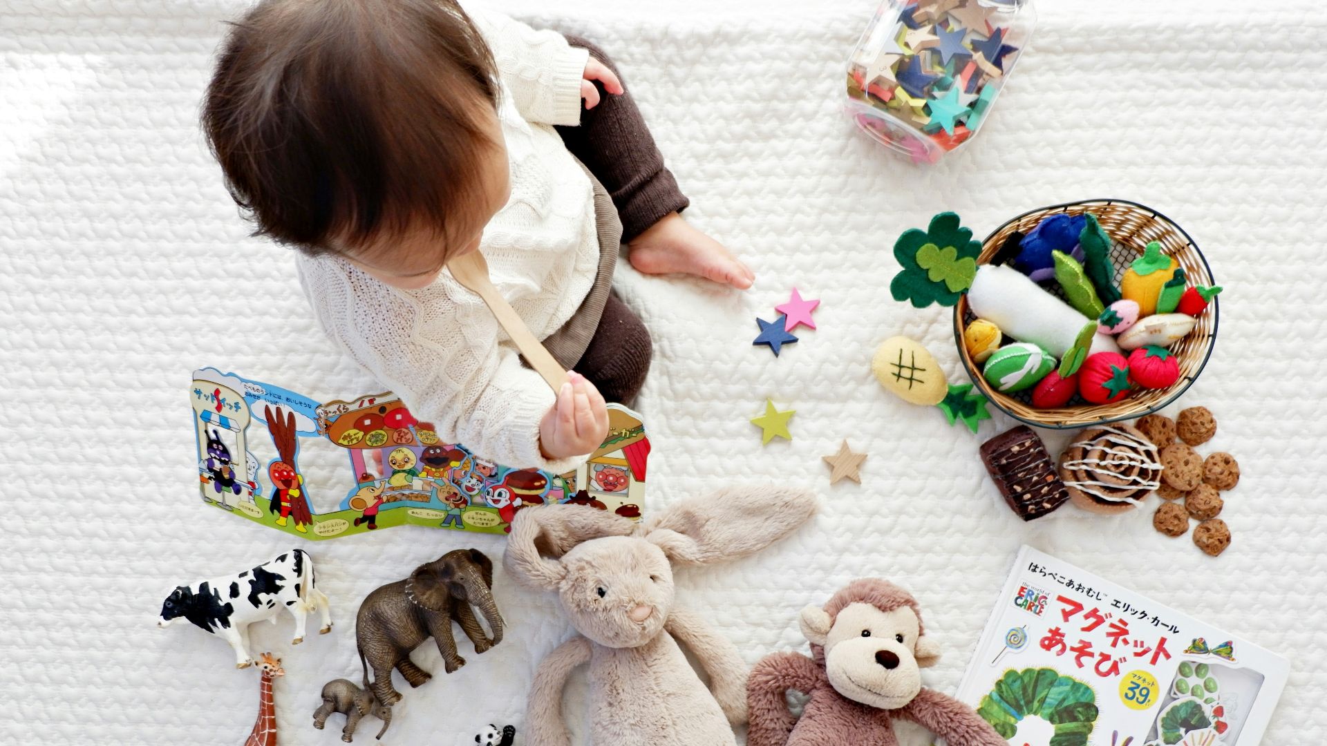 boy sitting on white cloth surrounded by toys