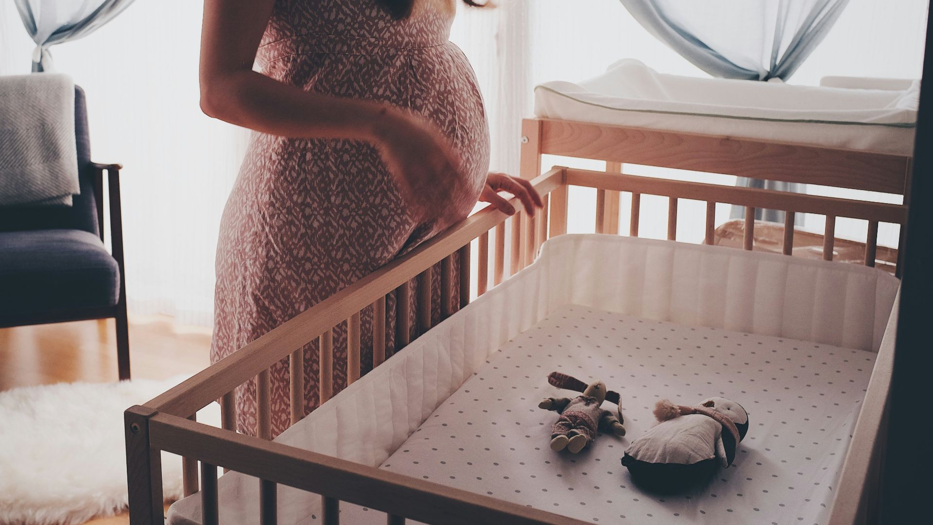 woman in white lace sleeveless dress standing beside brown wooden crib